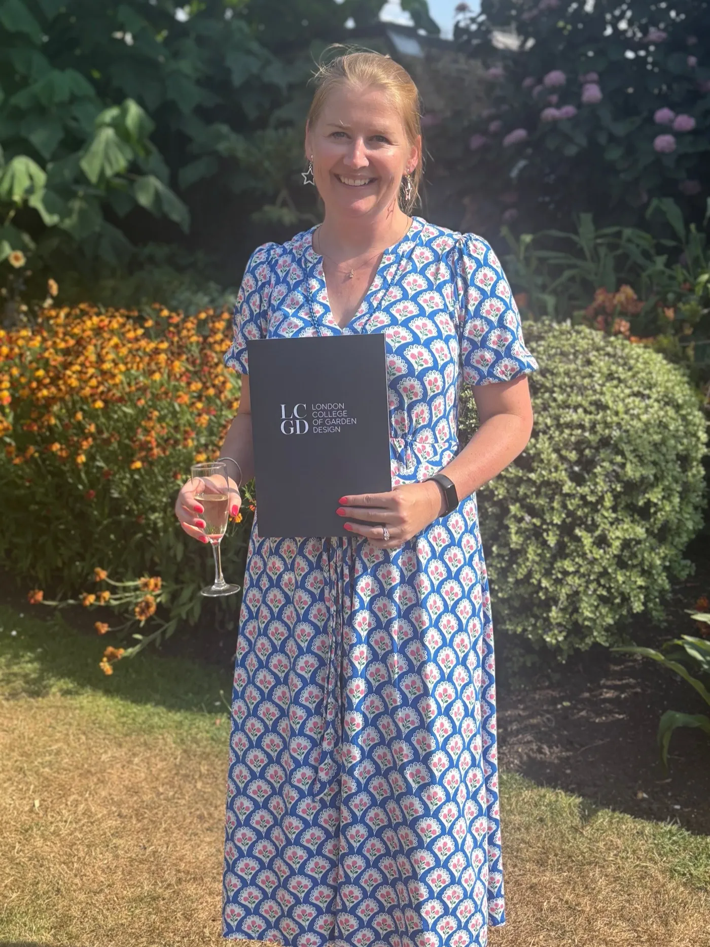 Jamie Maguire in a garden, holding her London College of Garden Design diploma folder
